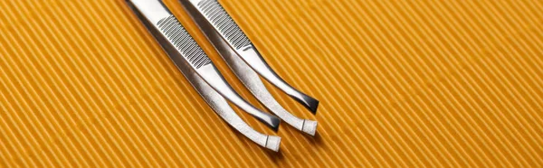 Stainless steel tweezers on yellow textured background, panoramic shot — Stock Photo