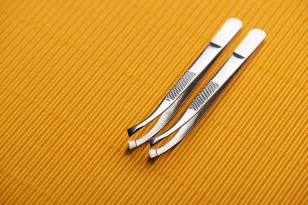 Stainless steel tweezers on yellow textured background — Stock Photo