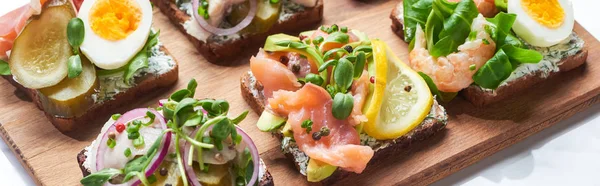 Panoramic shot of tasty smorrebrod sandwiches on wooden chopping board on white — Stock Photo