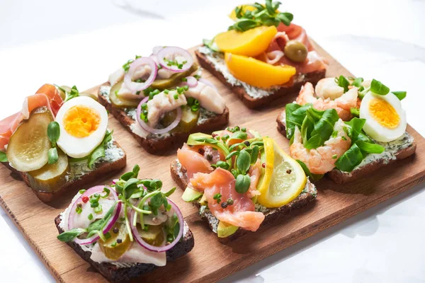 Sabrosos sándwiches de smorrebrod sobre tabla de cortar de madera en blanco - foto de stock