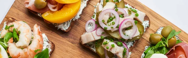Panoramic shot of delicious smorrebrod sandwiches on wooden chopping board on white — Stock Photo