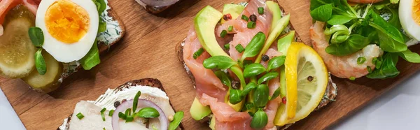 Panoramic shot of fresh smorrebrod sandwiches on wooden chopping board — Stock Photo