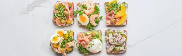 Panoramic shot of tasty smorrebrod sandwiches on white marble surface — Stock Photo