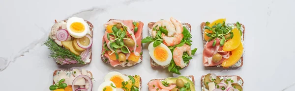 Panoramic shot of fresh and tasty smorrebrod sandwiches on white marble surface — Stock Photo