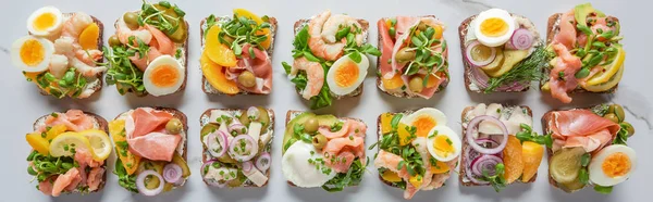 Tiro panorâmico de deliciosos sanduíches smorrebrod dinamarquês na superfície de mármore branco — Fotografia de Stock