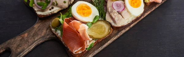 Panoramic shot of tasty smorrebrod sandwiches on wooden cutting board on grey surface — Stock Photo