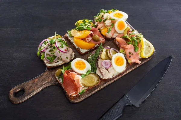 Wooden cutting board with danish smorrebrod sandwiches near knife on grey surface — Stock Photo