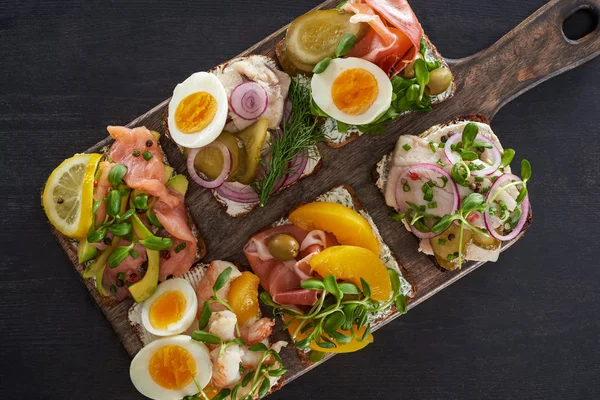 Top view of wooden cutting board with danish smorrebrod sandwiches on grey surface — Stock Photo