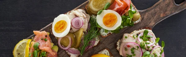 Panoramic shot of wooden cutting board with fresh danish smorrebrod sandwiches on grey surface — Stock Photo