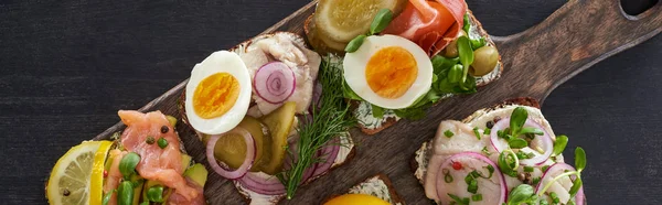 Panoramaaufnahme eines hölzernen Schneidebretts mit frischen dänischen Smorrebrod-Sandwiches auf grauer Oberfläche — Stockfoto