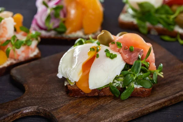 Selective focus of danish smorrebrod sandwich with poached egg near salmon on wooden cutting board — Stock Photo