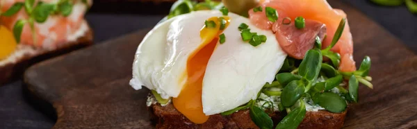 Plan panoramique du sandwich danois aux smorrebrods avec œuf poché près du saumon sur planche à découper en bois — Photo de stock