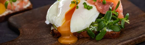 Panoramic shot of danish smorrebrod sandwich with poached egg near fresh salmon on wooden cutting board — Stock Photo