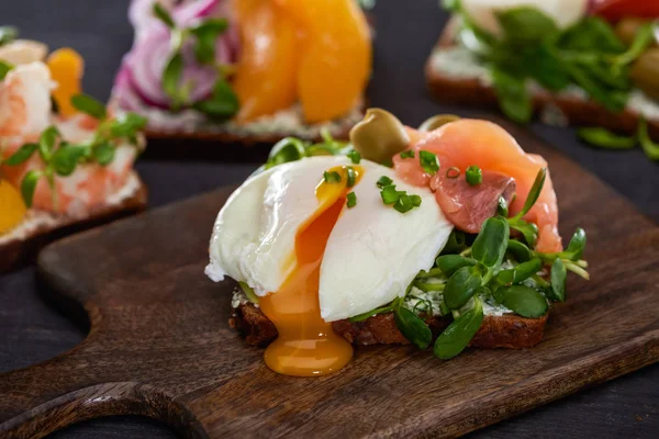 Nahaufnahme eines dänischen Smorrebrod-Sandwiches mit pochiertem Ei in der Nähe von frischem Lachs auf einem Holzschneidebrett — Stockfoto