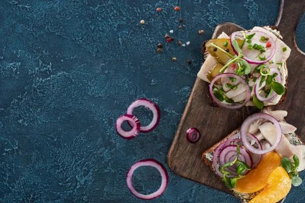 Vista superior de sabrosos sándwiches de smorrebrod en pan de centeno cerca de granos de pimienta en la superficie azul - foto de stock