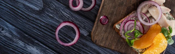 Panoramic shot of rye bread with tasty smorrebrod sandwich on blue wooden surface — Stock Photo