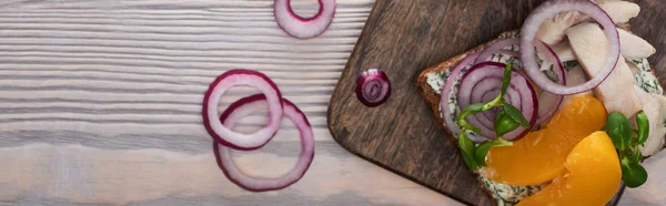 Panoramic shot of rye bread with tasty smorrebrod sandwich on wooden surface — Stock Photo