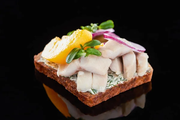 Close up of herring fish and canned peaches on prepared danish smorrebrod sandwich on black — Stock Photo