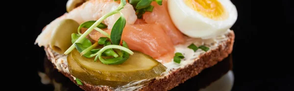 Panoramic shot of boiled egg near salmon on danish smorrebrod on black — Stock Photo