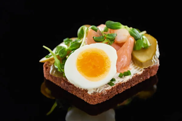 Nahaufnahme von gekochtem Ei in der Nähe von Lachs auf dänischem Smorrebrod-Sandwich auf Schwarz — Stockfoto