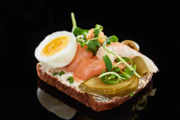 Nahaufnahme von gekochtem Ei in der Nähe von frischem Lachs auf dänischem Smorrebrod-Sandwich auf Schwarz — Stockfoto