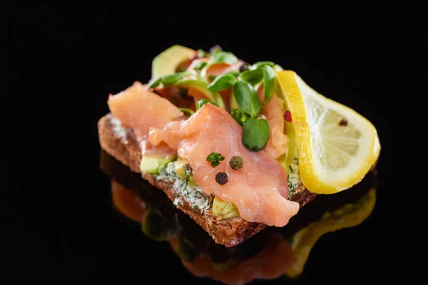 Primo piano di limone vicino a salmone su sandwich di smorrebrod danese su nero — Foto stock