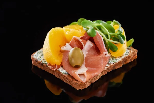 Selective focus of ham and canned peaches on smorrebrod sandwich on black — Stock Photo