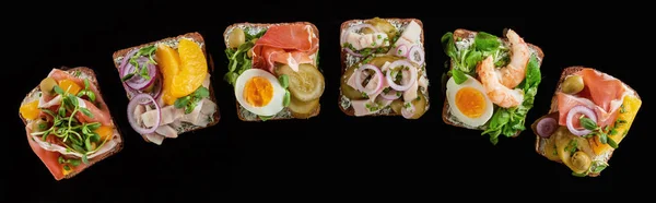 Panoramic shot of rye bread with prepared danish smorrebrod sandwiches isolated on black — Stock Photo