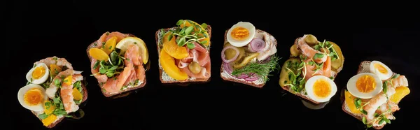 Panoramic shot of rye bread with prepared danish smorrebrod sandwiches isolated on black — Stock Photo