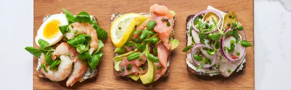 Plano panorámico de tabla de cortar de madera con smorrebrod sándwiches en la superficie de mármol blanco - foto de stock