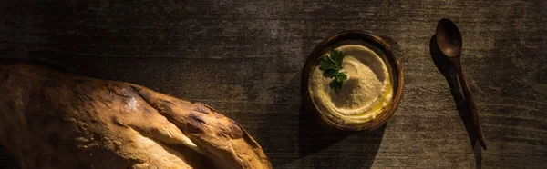 Top view of delicious hummus in bowl near fresh baked pita and spoon on wooden rustic table, panoramic shot — Stock Photo