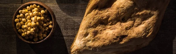 Vista superior de deliciosos grão de bico na tigela perto de pita cozido na mesa rústica de madeira, tiro panorâmico — Fotografia de Stock
