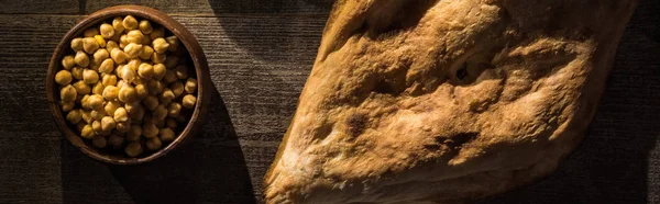 Vista dall'alto di deliziosi ceci in ciotola vicino alla pita appena sfornata su tavolo rustico in legno, colpo panoramico — Foto stock