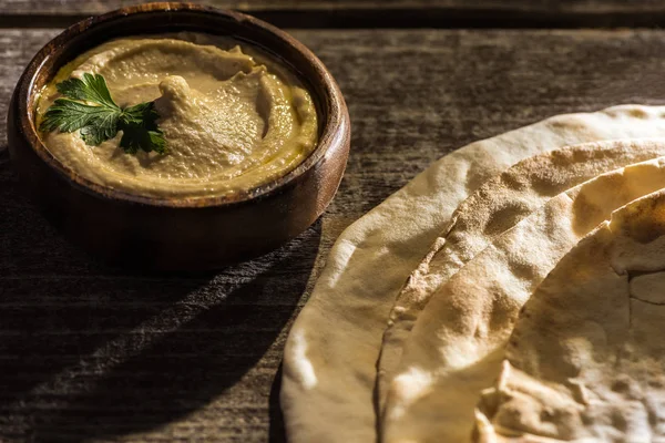 Délicieux houmous dans un bol près de pita fraîche cuite au four sur table rustique en bois — Photo de stock