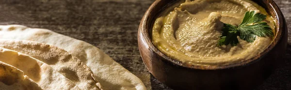 Delicious hummus in bowl near fresh baked pita on wooden rustic table, panoramic shot — Stock Photo