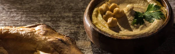 Nahaufnahme von köstlichem Hummus mit Kichererbsen in Schüssel in der Nähe von frisch gebackenem Fladenbrot auf rustikalem Holztisch, Panoramaaufnahme — Stockfoto