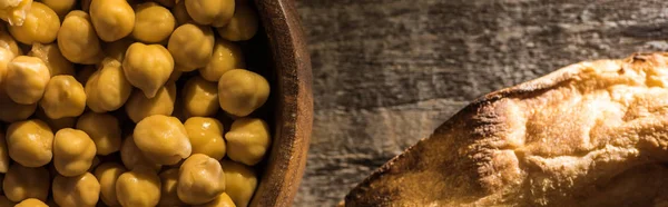 Vue du dessus des pois chiches dans un bol près d'une pita fraîche cuite au four sur une table rustique en bois, vue panoramique — Photo de stock