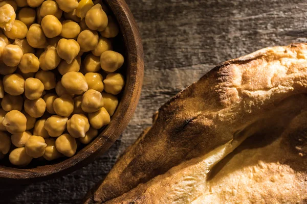 Top view of chickpeas in bowl near fresh baked pita on wooden rustic table — Stock Photo