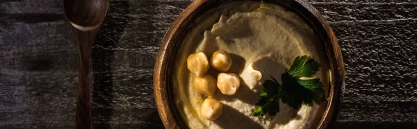 Vue de dessus de délicieux houmous aux pois chiches dans un bol sur une table rustique en bois, vue panoramique — Photo de stock