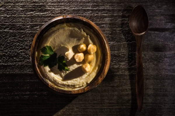 Vista superior de delicioso hummus com grão de bico na tigela em mesa rústica de madeira — Fotografia de Stock