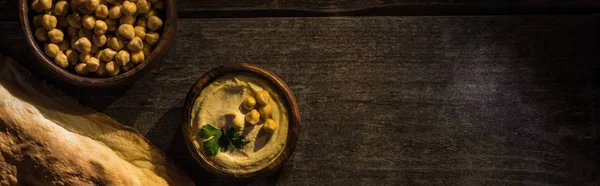 Vista superior de delicioso hummus com grão de bico em tigela perto de pita cozido na mesa rústica de madeira, tiro panorâmico — Fotografia de Stock