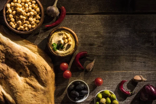 Vue de dessus de délicieux houmous, pois chiches, pita, épices et olives sur table rustique en bois — Photo de stock