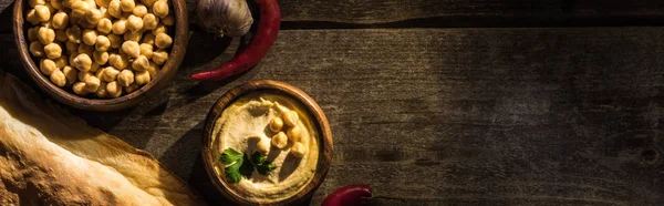 Draufsicht auf köstlichen Hummus, Kichererbsen, Flava, Gewürze auf rustikalem Holztisch, Panoramaaufnahme — Stockfoto