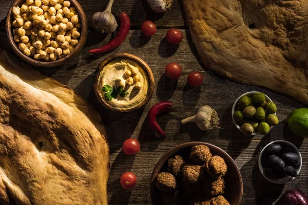 Vue de dessus de délicieux falafels, houmous, pois chiches, pita, légumes et olives sur table rustique en bois — Photo de stock