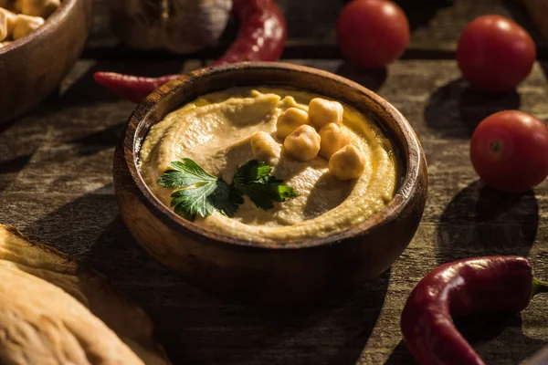 Delicious hummus, chickpeas, chili peppers and cherry tomatoes on wooden rustic table — Stock Photo