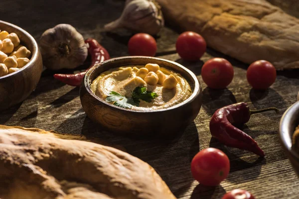 Delicious hummus, chickpeas, pita, vegetables and spices on wooden rustic table — Stock Photo
