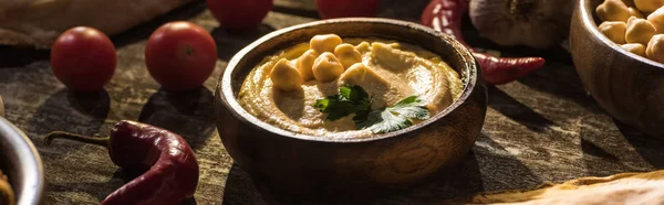 Delicious hummus, chickpeas, chili peppers and cherry tomatoes on wooden rustic table, panoramic shot — Stock Photo