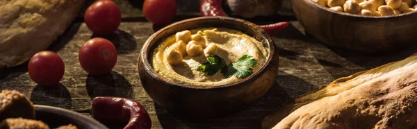 Delicioso hummus, garbanzos, pita, verduras y especias en la mesa rústica de madera, plano panorámico - foto de stock