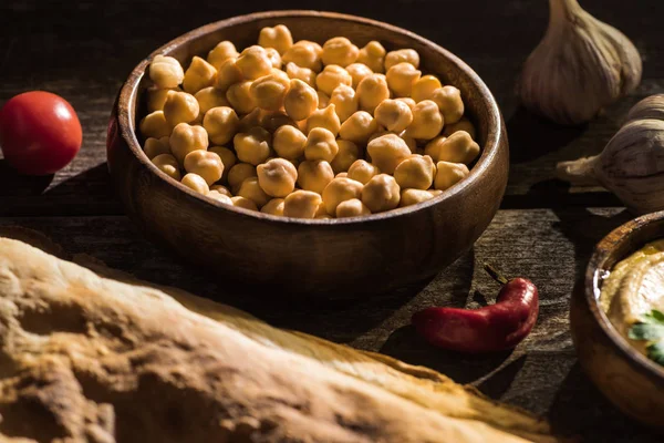 Köstliche Kichererbsen, Pita, Gemüse und Gewürze auf rustikalem Holztisch — Stockfoto