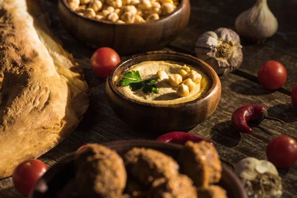 Selektiver Schwerpunkt von Falafel und köstlichem Hummus, Kichererbsen, Pita, Gemüse und Gewürzen auf rustikalem Holztisch — Stockfoto
